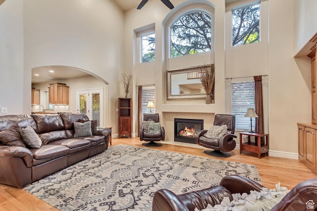 living room with a towering ceiling, light wood finished floors, a fireplace with flush hearth, a ceiling fan, and baseboards
