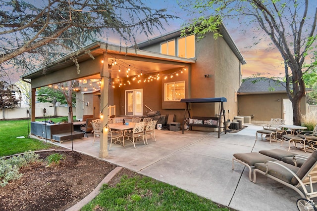 back of house at dusk with stucco siding, a patio area, an outdoor hangout area, and fence