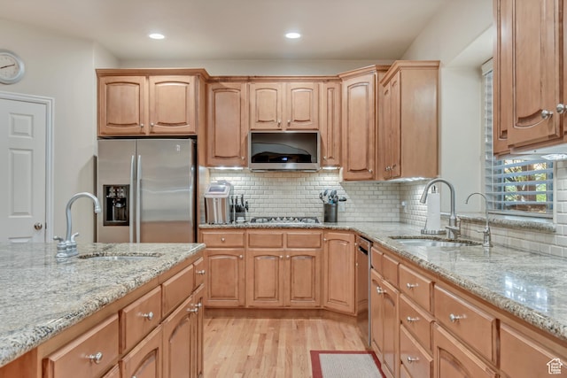 kitchen with appliances with stainless steel finishes, a sink, light stone counters, light wood-style flooring, and recessed lighting