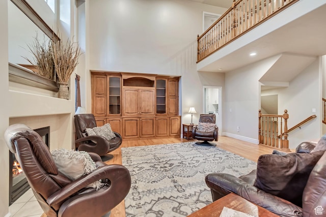 living area with a fireplace, a towering ceiling, light wood-style flooring, baseboards, and stairway