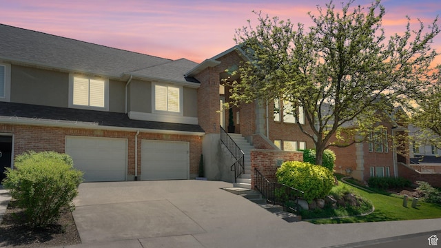 townhome / multi-family property with driveway, a garage, stairs, brick siding, and stucco siding
