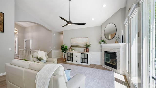 living area featuring ceiling fan, wood finished floors, a wainscoted wall, arched walkways, and a brick fireplace