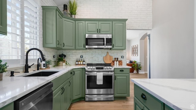 kitchen featuring appliances with stainless steel finishes, green cabinetry, a sink, and light wood-type flooring