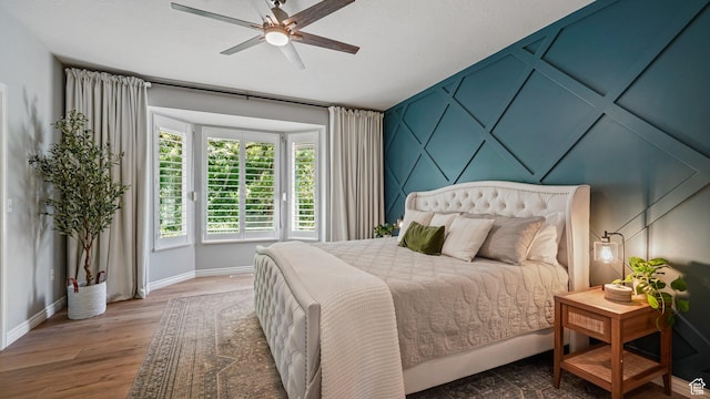 bedroom with baseboards, wood finished floors, a ceiling fan, and a decorative wall
