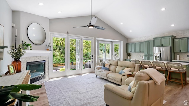 living area featuring high vaulted ceiling, light wood-style flooring, ceiling fan, recessed lighting, and a brick fireplace