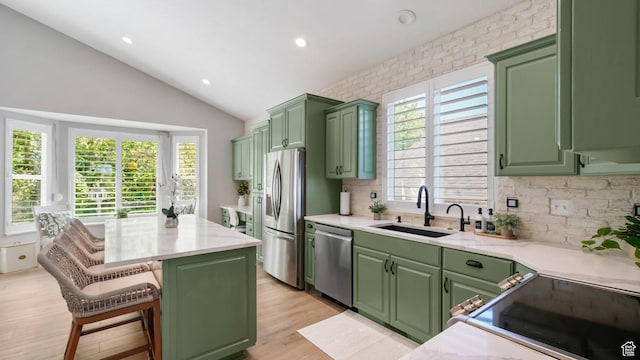 kitchen with a sink, green cabinetry, appliances with stainless steel finishes, decorative backsplash, and lofted ceiling