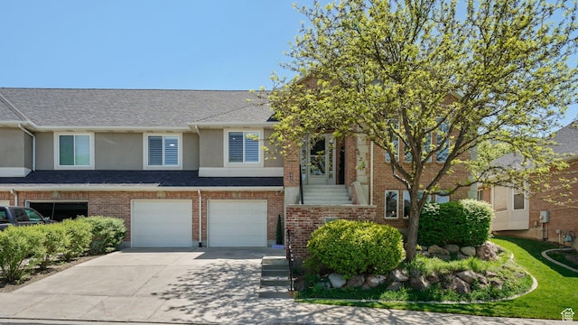 townhome / multi-family property featuring concrete driveway, an attached garage, stucco siding, a shingled roof, and brick siding