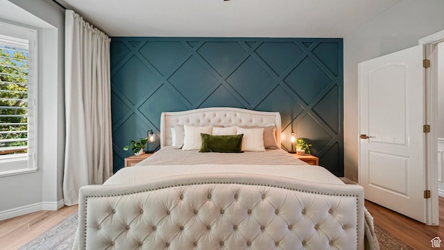 bedroom featuring a decorative wall, baseboards, and light wood-type flooring