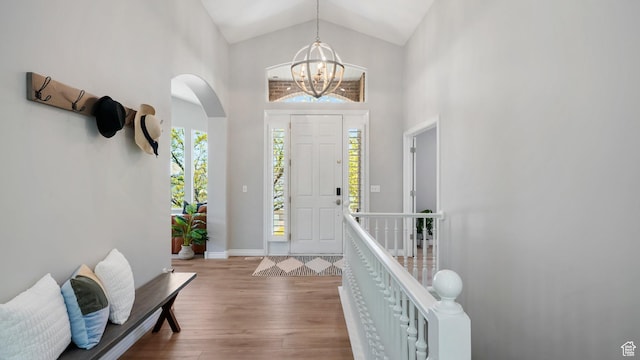 foyer entrance featuring wood finished floors, arched walkways, high vaulted ceiling, a chandelier, and baseboards