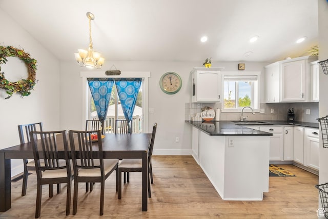 kitchen with dark countertops, a sink, white cabinetry, a chandelier, and decorative backsplash