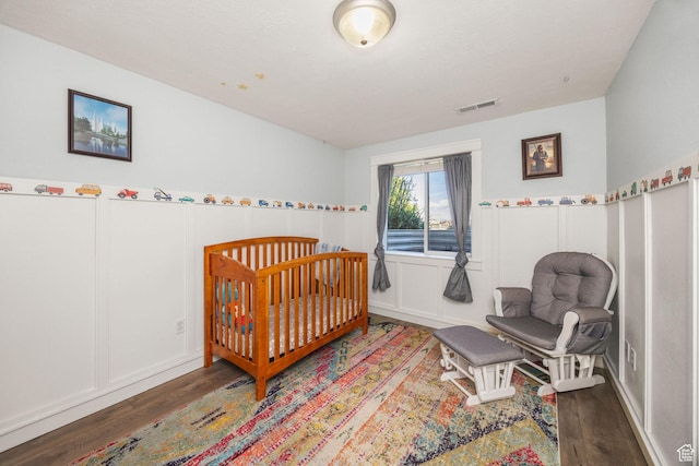 bedroom with wood finished floors, a decorative wall, and wainscoting