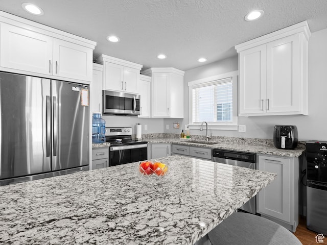 kitchen with appliances with stainless steel finishes, a sink, recessed lighting, light stone countertops, and white cabinetry