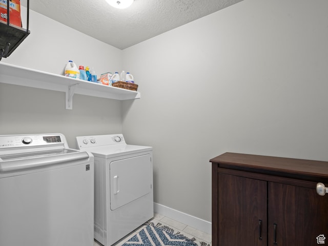 laundry area featuring independent washer and dryer, light tile patterned floors, a textured ceiling, and baseboards