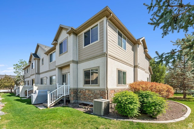 back of property with central AC unit, stone siding, a lawn, and stucco siding