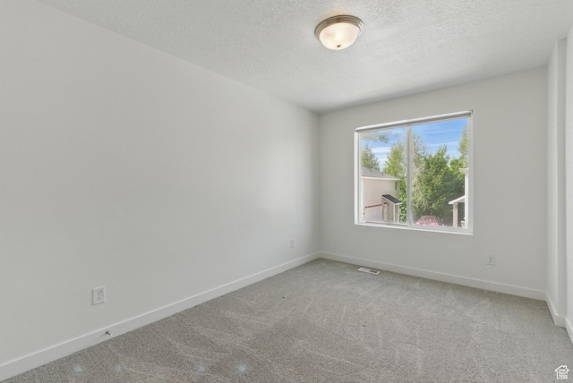 carpeted spare room featuring a textured ceiling and baseboards