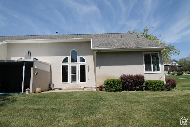 rear view of property with stucco siding, a lawn, roof with shingles, and entry steps