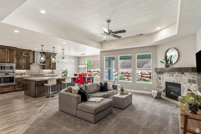 750 W 1860 N, Washington, UT 84780 - living room featuring a raised ceiling, a ceiling fan, a textured ceiling, baseboards, and a stone fireplace