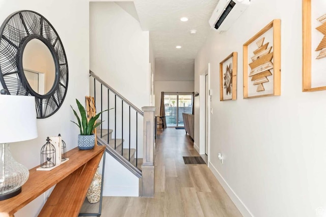 hall featuring wood finished floors, a wall mounted AC, recessed lighting, stairs, and baseboards
