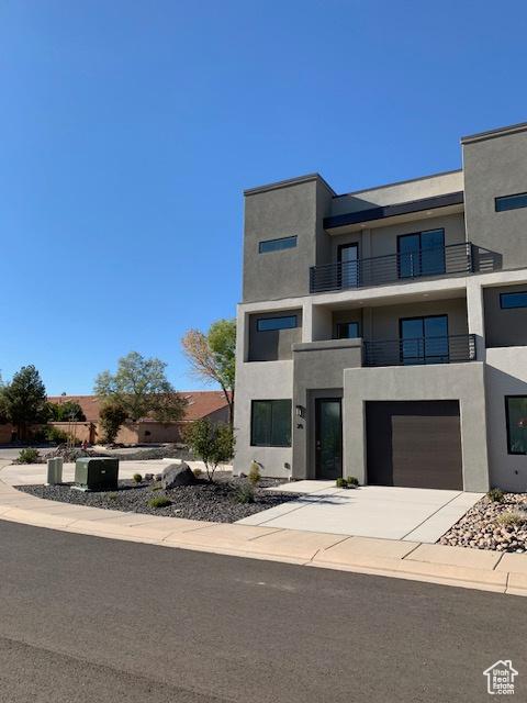 view of front of home featuring stucco siding, a balcony, an attached garage, and concrete driveway