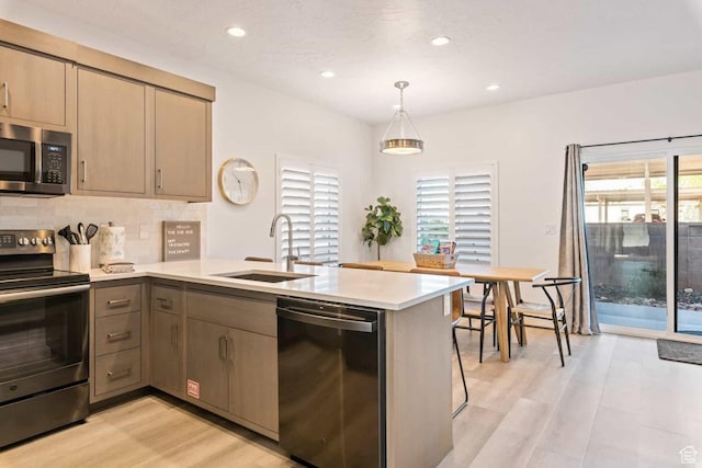 kitchen with appliances with stainless steel finishes, a sink, a peninsula, light wood finished floors, and recessed lighting