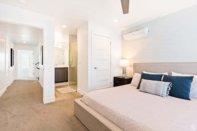 bedroom featuring an AC wall unit, light colored carpet, ensuite bathroom, baseboards, and recessed lighting