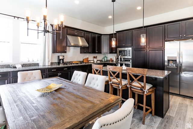 5502 N Valley Rd W, Lehi, UT 84043 - kitchen featuring appliances with stainless steel finishes, under cabinet range hood, a chandelier, an island with sink, and light stone countertops