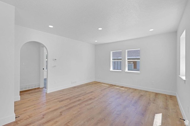 empty room with arched walkways, light wood finished floors, recessed lighting, and baseboards