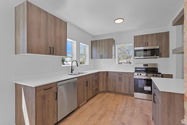 kitchen with appliances with stainless steel finishes, a sink, light wood-style flooring, light countertops, and brown cabinetry