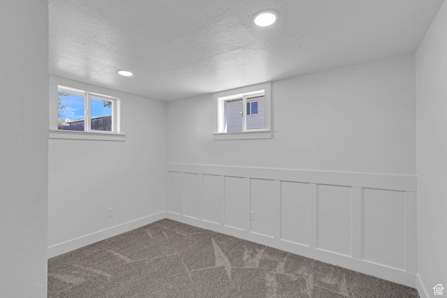 basement featuring a textured ceiling, carpet flooring, a wainscoted wall, recessed lighting, and a decorative wall