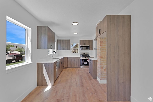 kitchen with appliances with stainless steel finishes, a sink, light wood-type flooring, light countertops, and recessed lighting