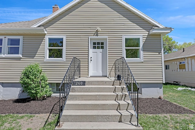 bungalow-style home with a chimney and roof with shingles