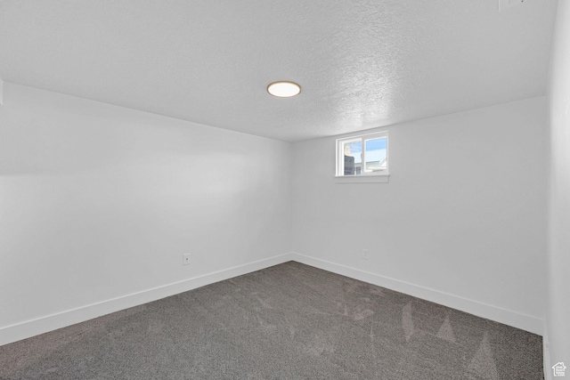 basement featuring a textured ceiling, dark carpet, and baseboards