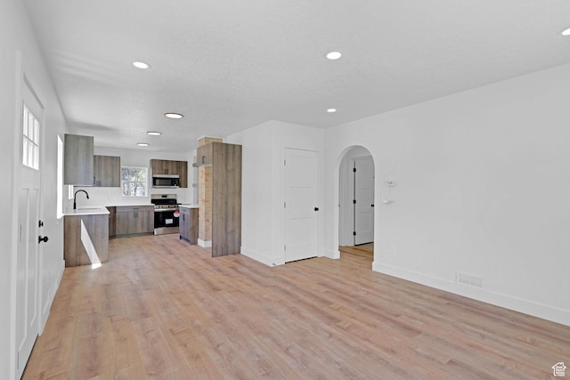 unfurnished living room featuring recessed lighting, arched walkways, light wood-style flooring, and baseboards