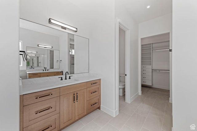 full bath with toilet, vanity, baseboards, and a walk in closet