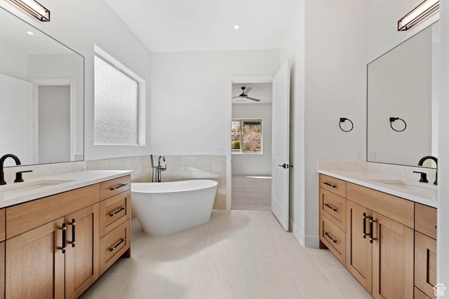 full bathroom with two vanities, a freestanding bath, ceiling fan, tile walls, and tile patterned flooring