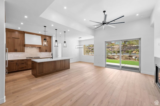 kitchen featuring open floor plan, light countertops, stainless steel gas stovetop, custom exhaust hood, and recessed lighting