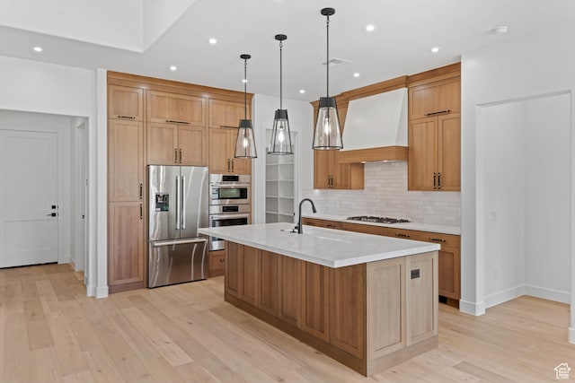 kitchen featuring appliances with stainless steel finishes, premium range hood, a sink, backsplash, and light wood-style flooring