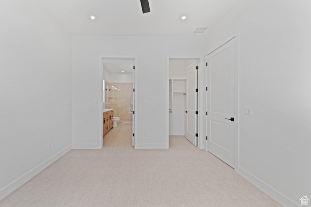 unfurnished bedroom with a walk in closet, light colored carpet, recessed lighting, baseboards, and connected bathroom