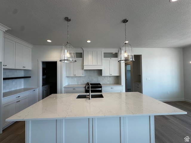 kitchen featuring dark wood-type flooring, decorative backsplash, white cabinetry, a kitchen island with sink, and a sink
