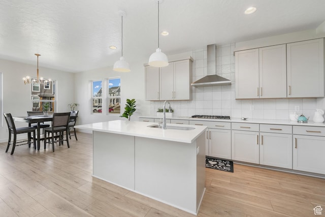 kitchen featuring wall chimney exhaust hood, a sink, light countertops, light wood-style floors, and a chandelier