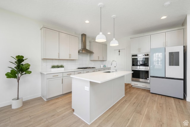 kitchen featuring stainless steel appliances, wall chimney exhaust hood, backsplash, light wood-type flooring, and recessed lighting