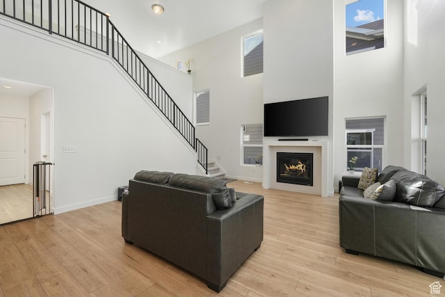 living area with a towering ceiling, healthy amount of natural light, light wood-style floors, and a tile fireplace