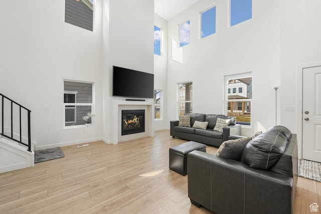 living room with a towering ceiling, light wood-style floors, a glass covered fireplace, baseboards, and stairs
