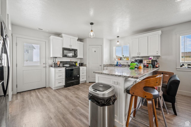2460 W 450 N Unit 7, Tremonton, UT 84337 - kitchen featuring black appliances, a peninsula, light wood finished floors, a kitchen breakfast bar, and white cabinets