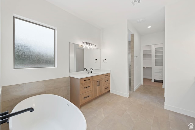 full bathroom featuring a spacious closet, a freestanding bath, vanity, and tile patterned floors