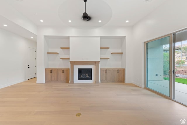 unfurnished living room featuring light wood-style flooring, recessed lighting, baseboards, built in features, and a glass covered fireplace