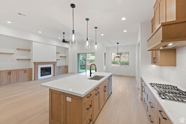 kitchen featuring a sink, light wood-style floors, recessed lighting, a glass covered fireplace, and a kitchen island with sink