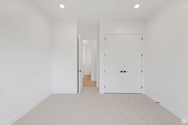 unfurnished bedroom with light colored carpet, baseboards, a closet, and recessed lighting