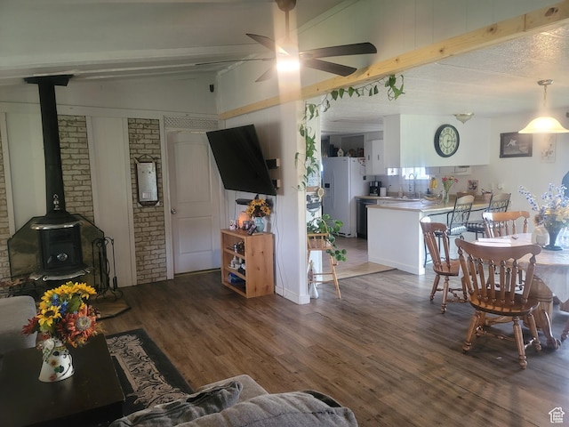living area featuring a wood stove, beam ceiling, wood finished floors, a ceiling fan, and brick wall