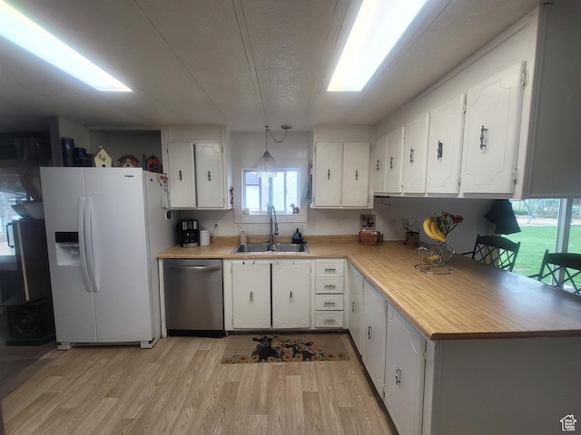kitchen featuring white fridge with ice dispenser, stainless steel dishwasher, a sink, light countertops, and light wood-type flooring